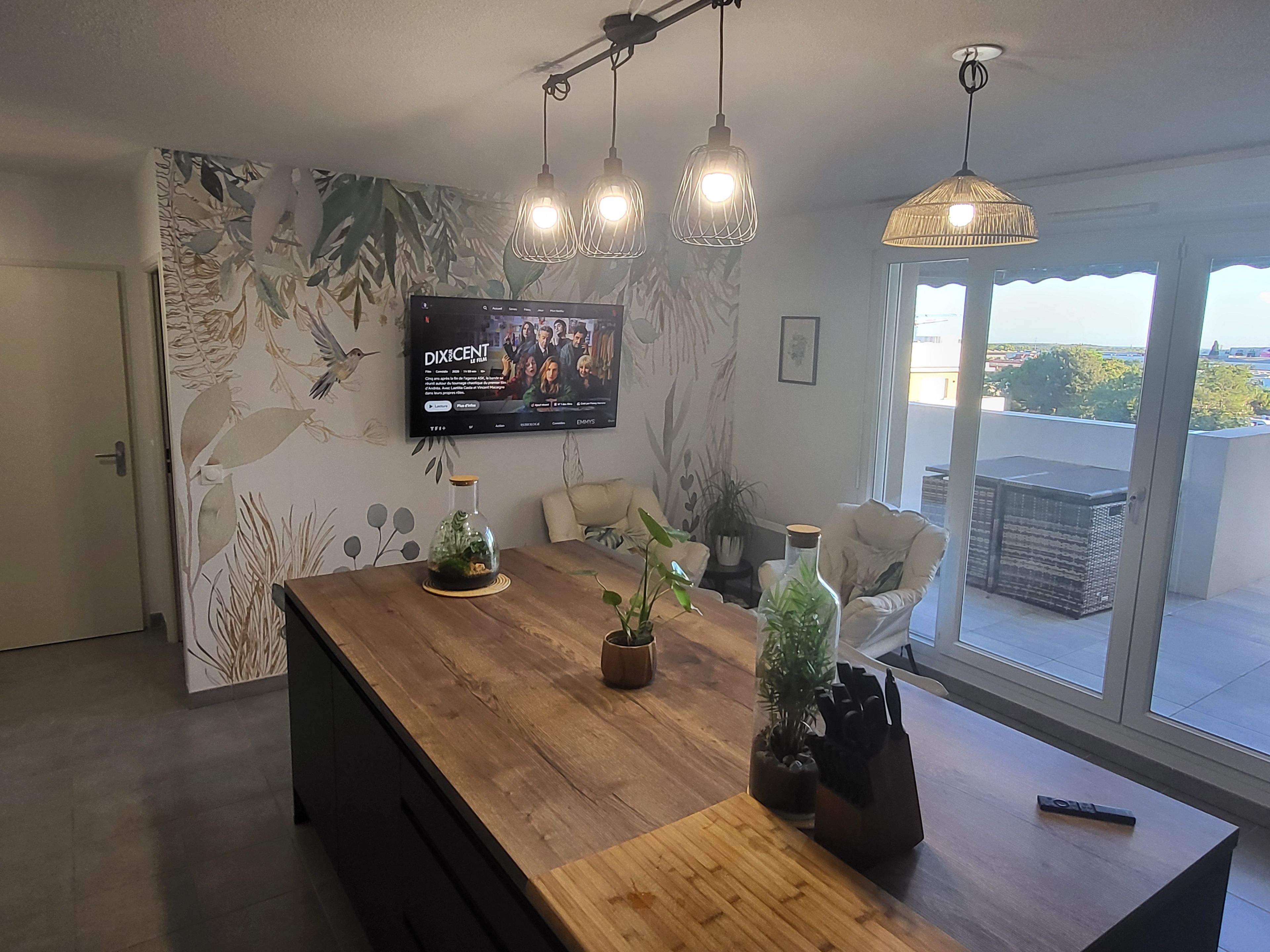 Una cucina moderna con isola in legno, TV a schermo piatto montata a parete e un'ampia finestra che offre vista sull'esterno.