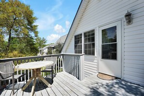 Une terrasse avec une table ronde et des chaises, un mur extérieur blanc et une grande fenêtre.