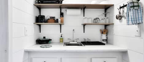 Cozinha compacta com armários brancos, pia e diversos utensílios e eletrodomésticos.