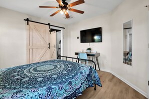 Ein Schlafzimmer mit Bett, Schreibtisch, Stuhl, Deckenventilator, Fernseher und Kleiderschrank.