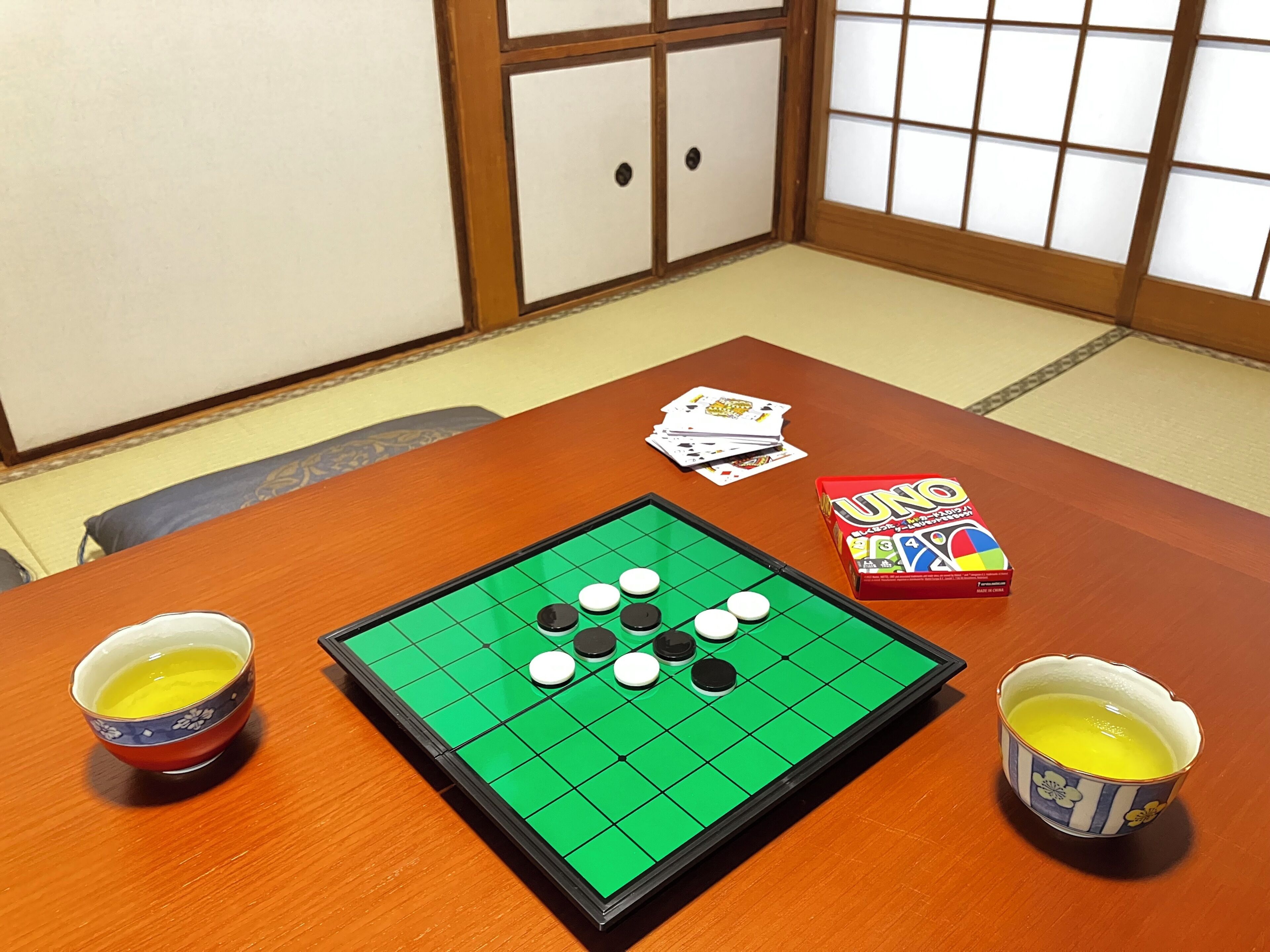Una habitación con suelo de tatami, un panel shoji, una mesa con un tablero de juego, cartas y una caja de UNO.