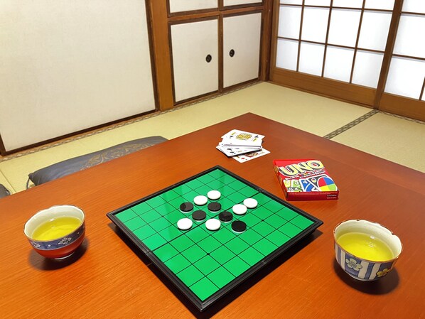 Una habitación con suelo de tatami, un panel shoji, una mesa con un tablero de juego, cartas y una caja de UNO.