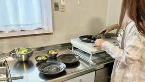 A kitchen with a stove, a bowl of salad, and a person cooking. - Entire 85-square-meter Property for Rent | Experience Traditional Japanese-Style Rooms | 5 minutes from Shin-Osaka, 38 minutes direct to Kyoto | A base for sightseeing in the Kansai region near a shopping district (大阪市)