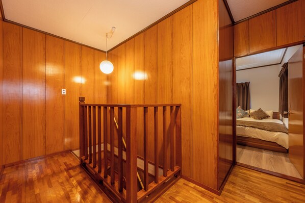 A room with wooden panel walls, a wooden railing, and a bed with pillows and a blanket. - Entire 85-square-meter Property for Rent | Experience Traditional Japanese-Style Rooms | 5 minutes from Shin-Osaka, 38 minutes direct to Kyoto | A base for sightseeing in the Kansai region near a shopping district (大阪市)