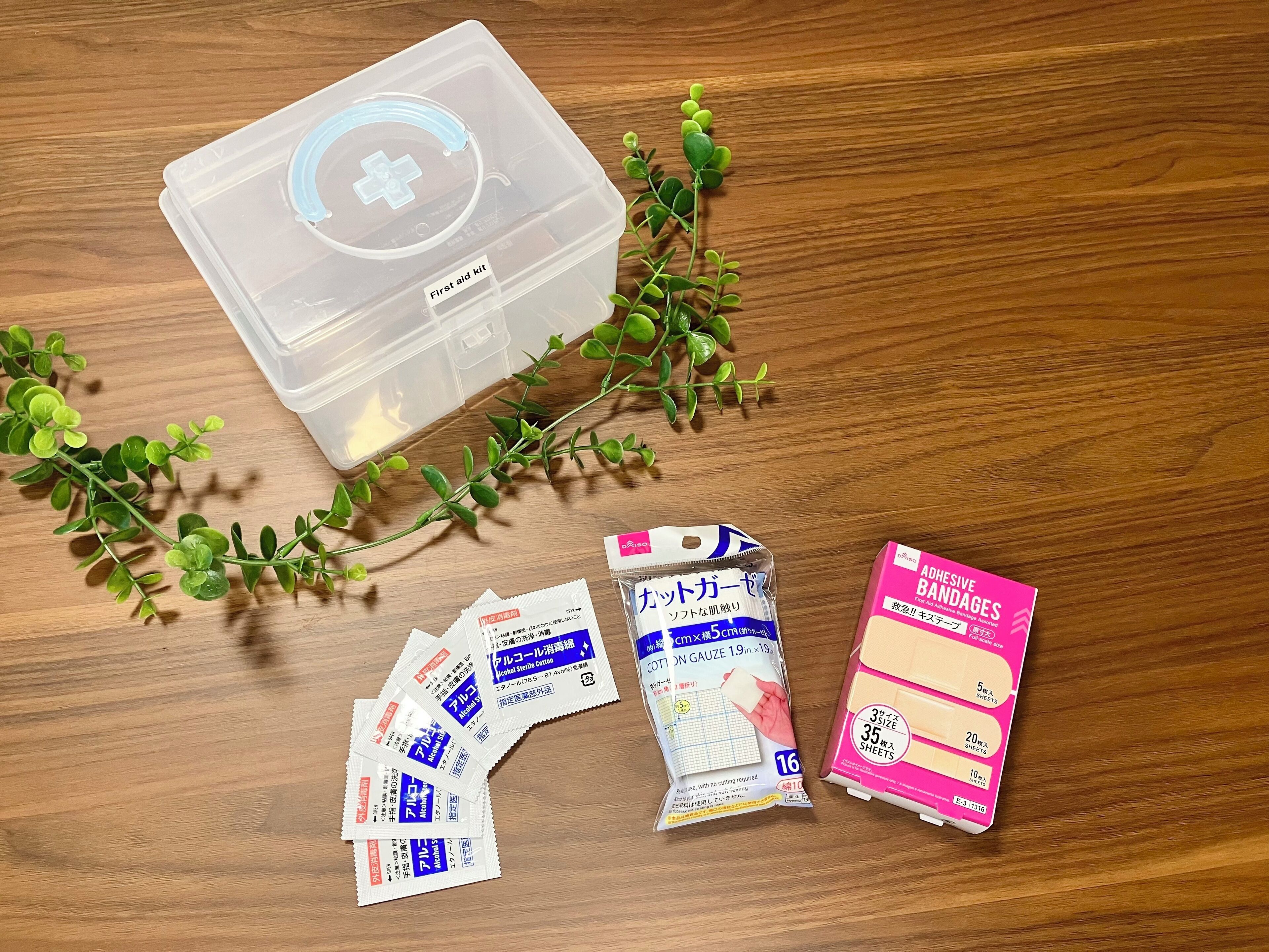 A first aid kit, cotton gauze, alcohol swabs, adhesive bandages, and a small plant on a wooden surface.