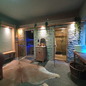 A spa room with a stone wall, a wooden bench, a glass shower enclosure, and a fur rug. - Alsace apartment adjacent to the Domaine de Pairis, Pets allowed, (Orbey)