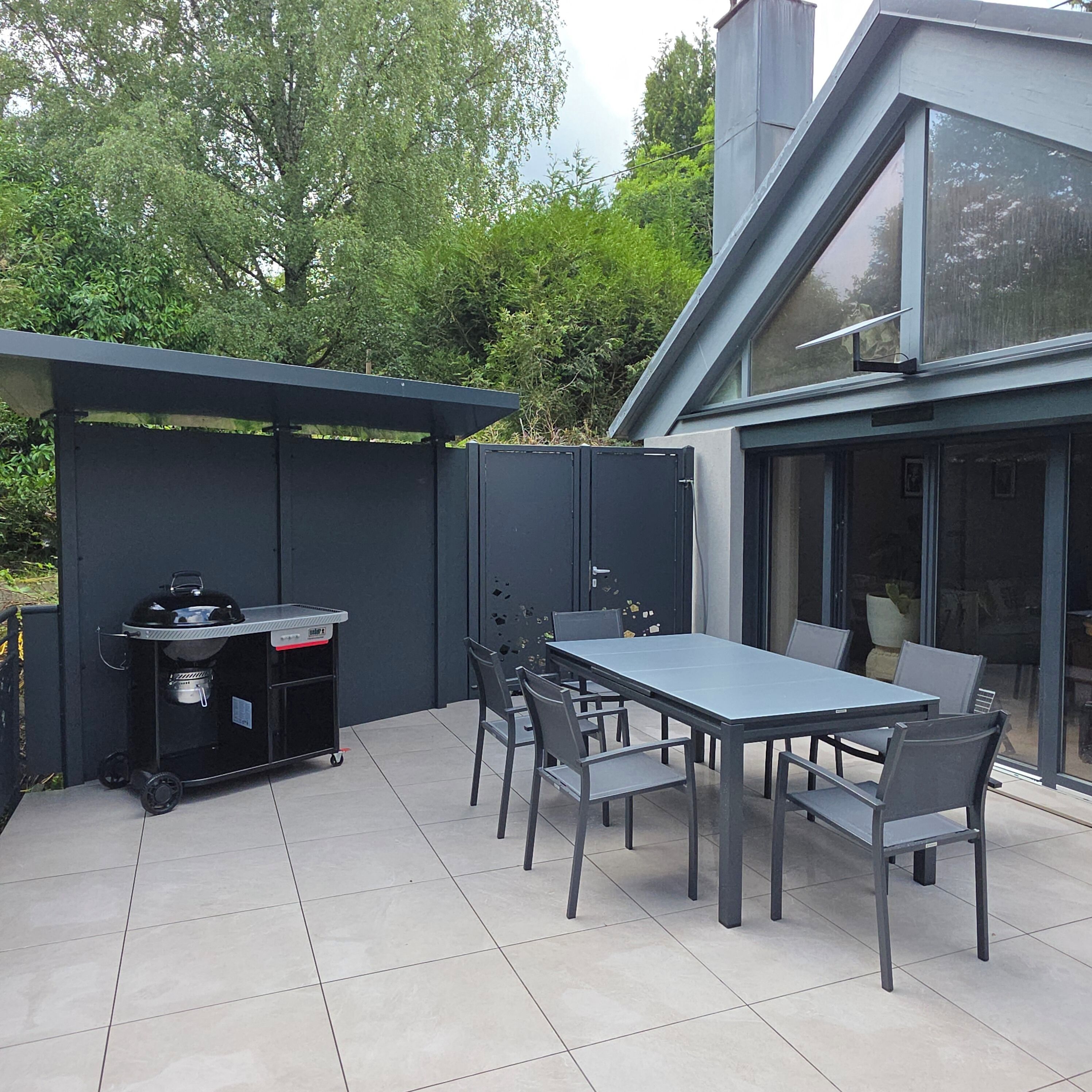 A patio with a table and chairs, a grill, and a glass-enclosed area.