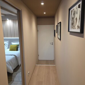 Um corredor com uma cama, uma porta e quadros na parede.