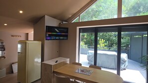 A modern kitchen with a built-in refrigerator, a dining area with a table and chairs, and a large window providing a view of the outdoors. - Alsace apartment adjacent to the Domaine de Pairis, Pets allowed, (Orbey)