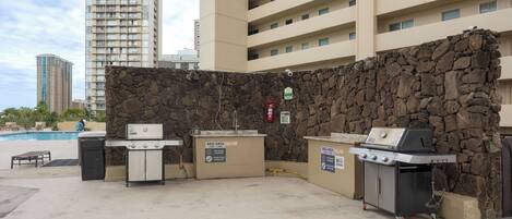 An outdoor BBQ area with stone walls, a pool, and high-rise buildings in the background.