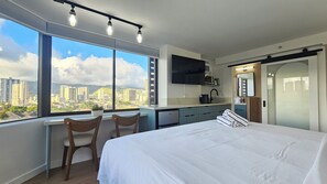 Ein Hotelzimmer mit einem großen Bett, einem Schreibtisch mit zwei Stühlen, einem Fernseher, einer Mikrowelle und Blick auf die Stadt.