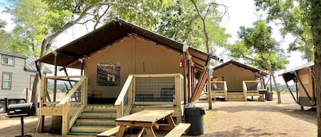 A campsite with wooden cabins, picnic tables, and a fenced area.