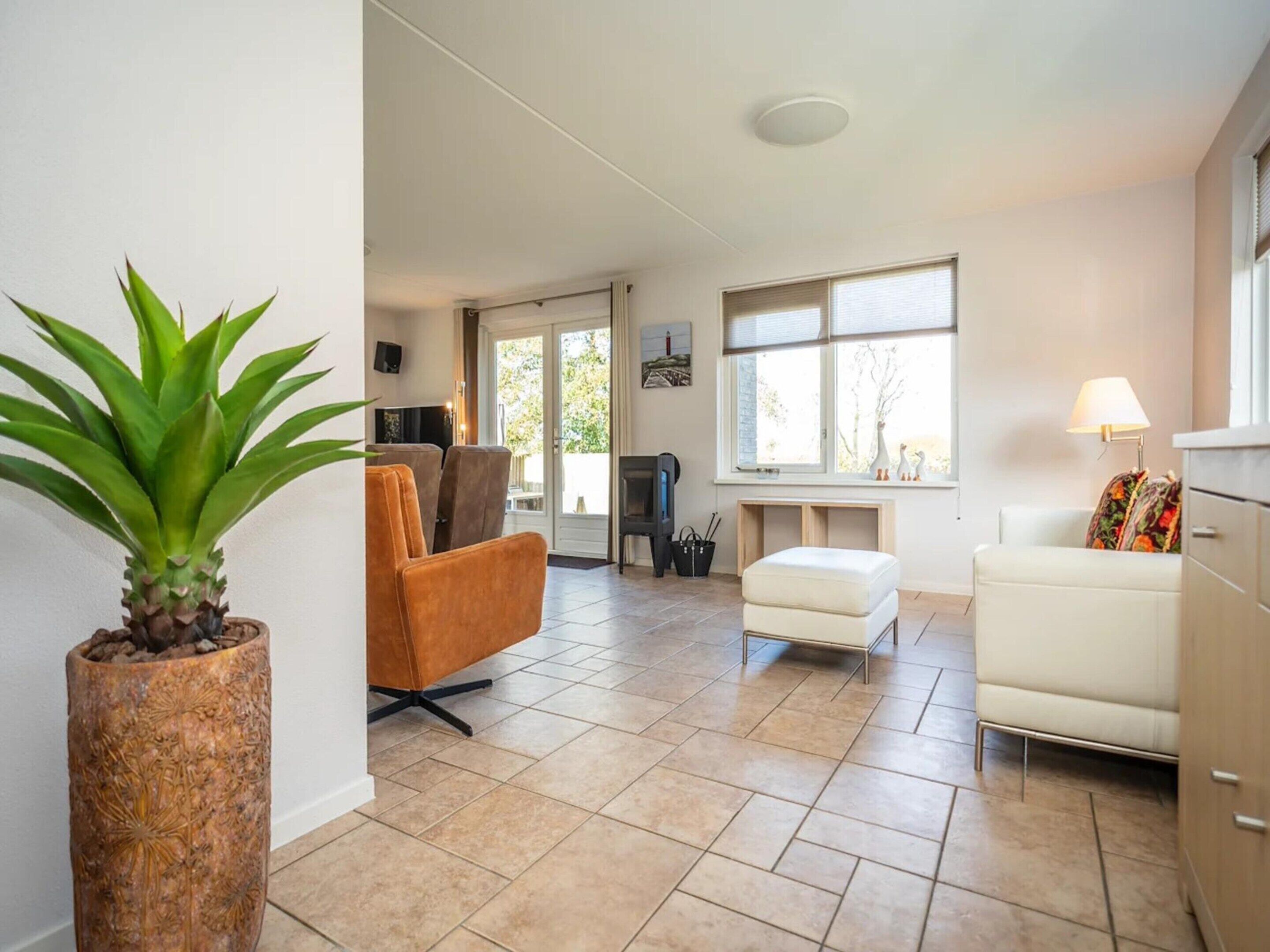 A modern living room with a sofa, armchair, and ottoman, a potted plant, and a television.