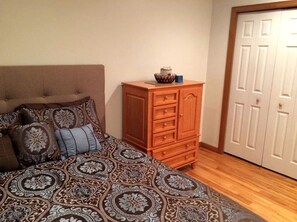 A bedroom with a bed, patterned bedding, a wooden dresser, and a white closet.
