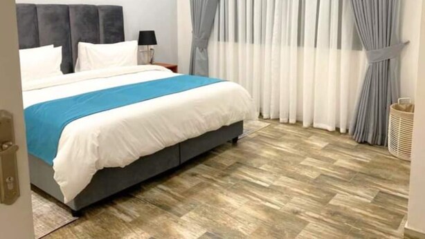 A bedroom with a bed, curtains, a nightstand, and a wall-mounted lamp. - Apartment in Roma (Lusaka)