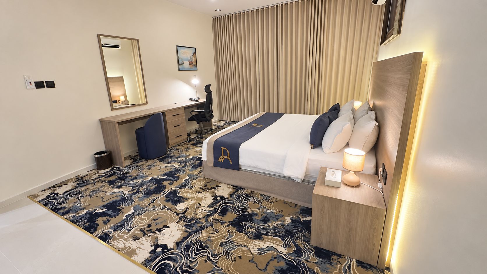 Quarto de hotel com cama, mesa de cabeceira, escrivaninha, cadeira e uma grande janela com cortinas.