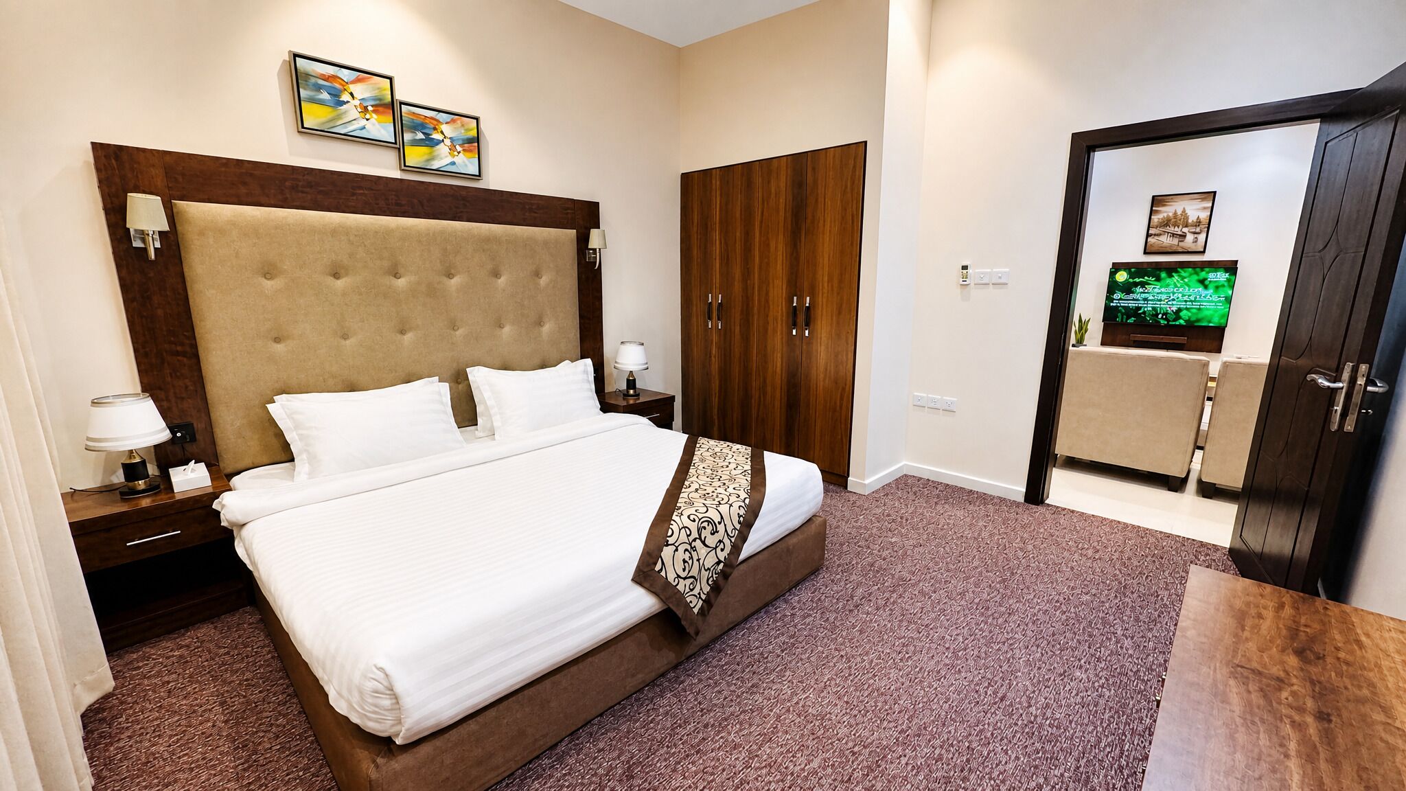 A hotel room with a large bed, a wardrobe, a television, and artwork on the wall.