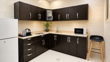 A modern kitchen with dark cabinets, a white refrigerator, a microwave, a sink, and a small stool.