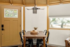A dining area with a wooden table, black chairs, a decorative wall hanging, and a view through a window. - Rustic Western Cabin with Loft & Hot Tub Located Near Canyon Lake, Texas (Canyon Lake)