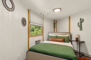 A bedroom with a bed, a window, a bedside table, and wall art. - Rustic Western Cabin with Loft & Hot Tub Located Near Canyon Lake, Texas (Canyon Lake)