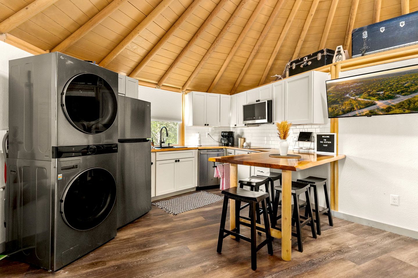 A compact kitchen with a washing machine, a microwave, and a wooden dining area.