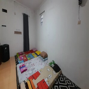 A room with a bed, a window with curtains, a wall-mounted light switch, and a power outlet. - Cozzy Darmaga Palayangan Pangalengan (pangalengan)