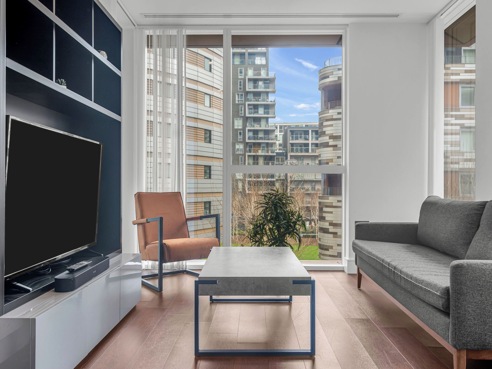 A modern living room with a flat-screen TV, a sofa, a chair, and a coffee table.