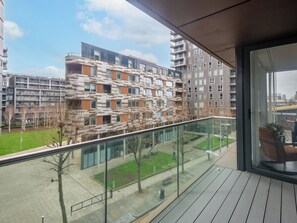 A balcony with a view of modern apartment buildings, a glass railing, and a potted plant. - Canary Heights 2bed by Interhome (London)