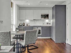 A modern kitchen with grey cabinets, a built-in oven, and a microwave. - Canary Heights 2bed by Interhome (London)