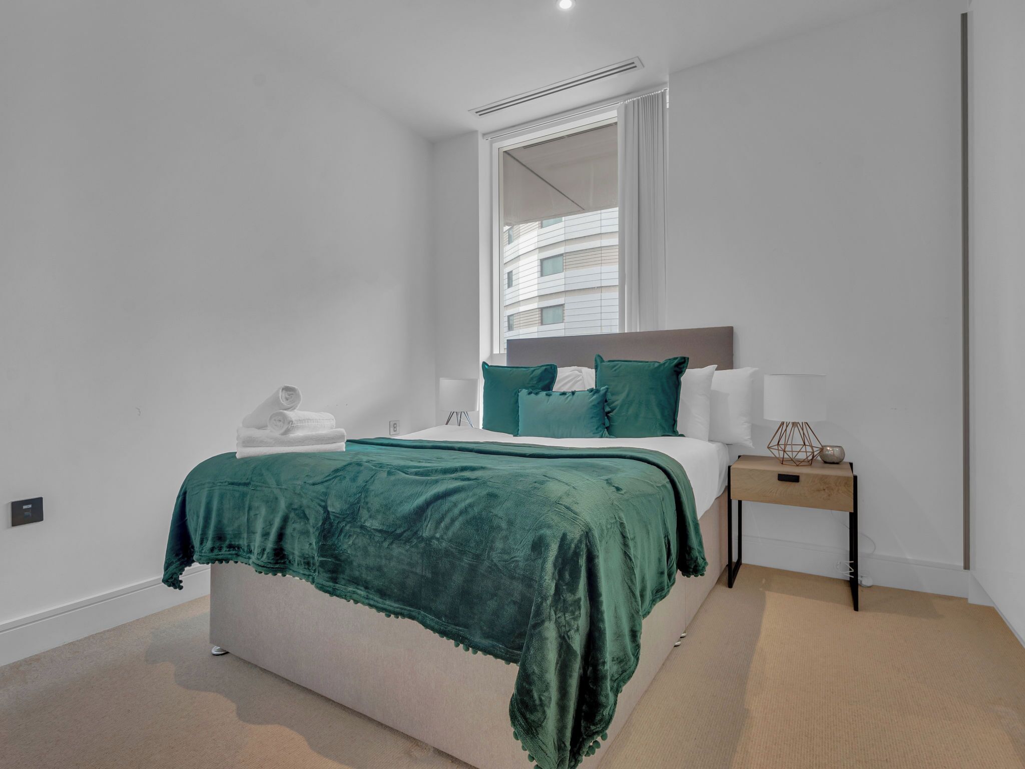 A modern bedroom with a bed, a bedside table, and a window.