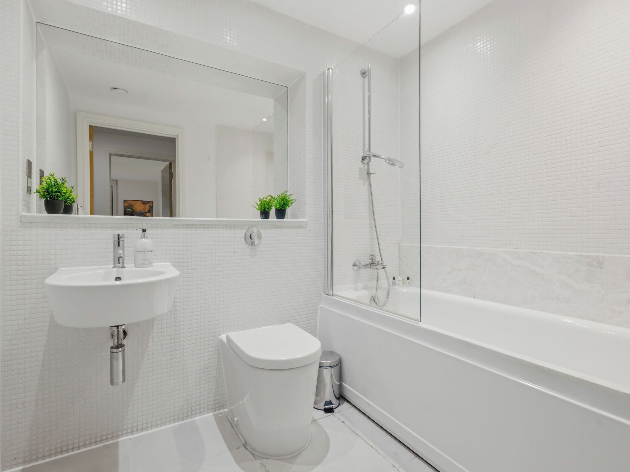 Un baño moderno con lavamanos blanco, inodoro y ducha con mampara de vidrio.