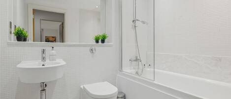Un baño moderno con lavamanos blanco, inodoro y ducha con mampara de vidrio.