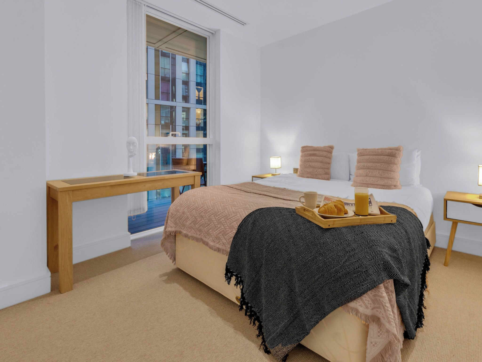 A bedroom with a bed, bedside tables, a window with a view, and a tray with breakfast items.