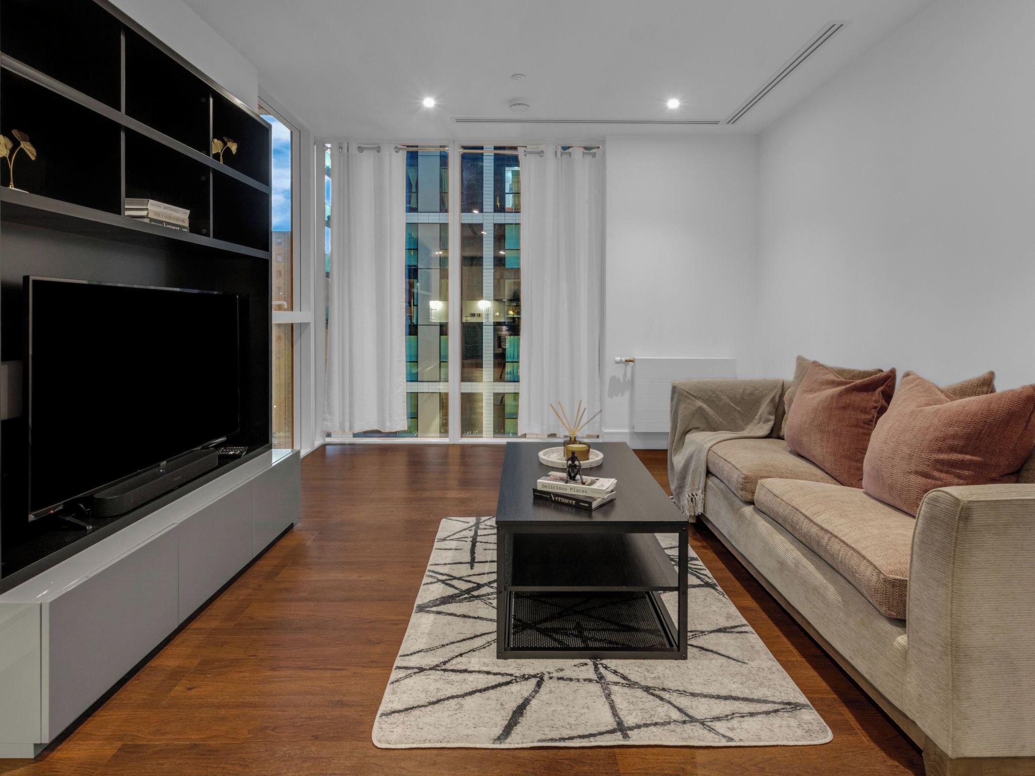 A modern living room with a flat-screen TV, a sofa, a coffee table, and a patterned rug.