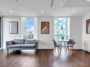 A modern living room with a grey sofa, a dining table with two chairs, large windows with city views, and artwork on the walls. - Canary Heights 2bed by Interhome (London)