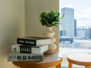 A stack of books on a wooden table with a view of a cityscape through a window. - Stratford Loft by Interhome (London East)
