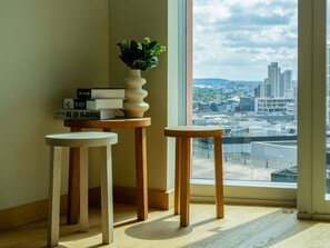 A room with a view of a cityscape through a large window, a small table with a potted plant, and a stack of books on a shelf. - Stratford Loft by Interhome (London East)
