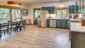 A modern kitchen with a dining area, featuring a large island, stainless steel appliances, and green cabinetry. - NEW! Riverfront Trout Fishing White River Ozarks (Cotter)