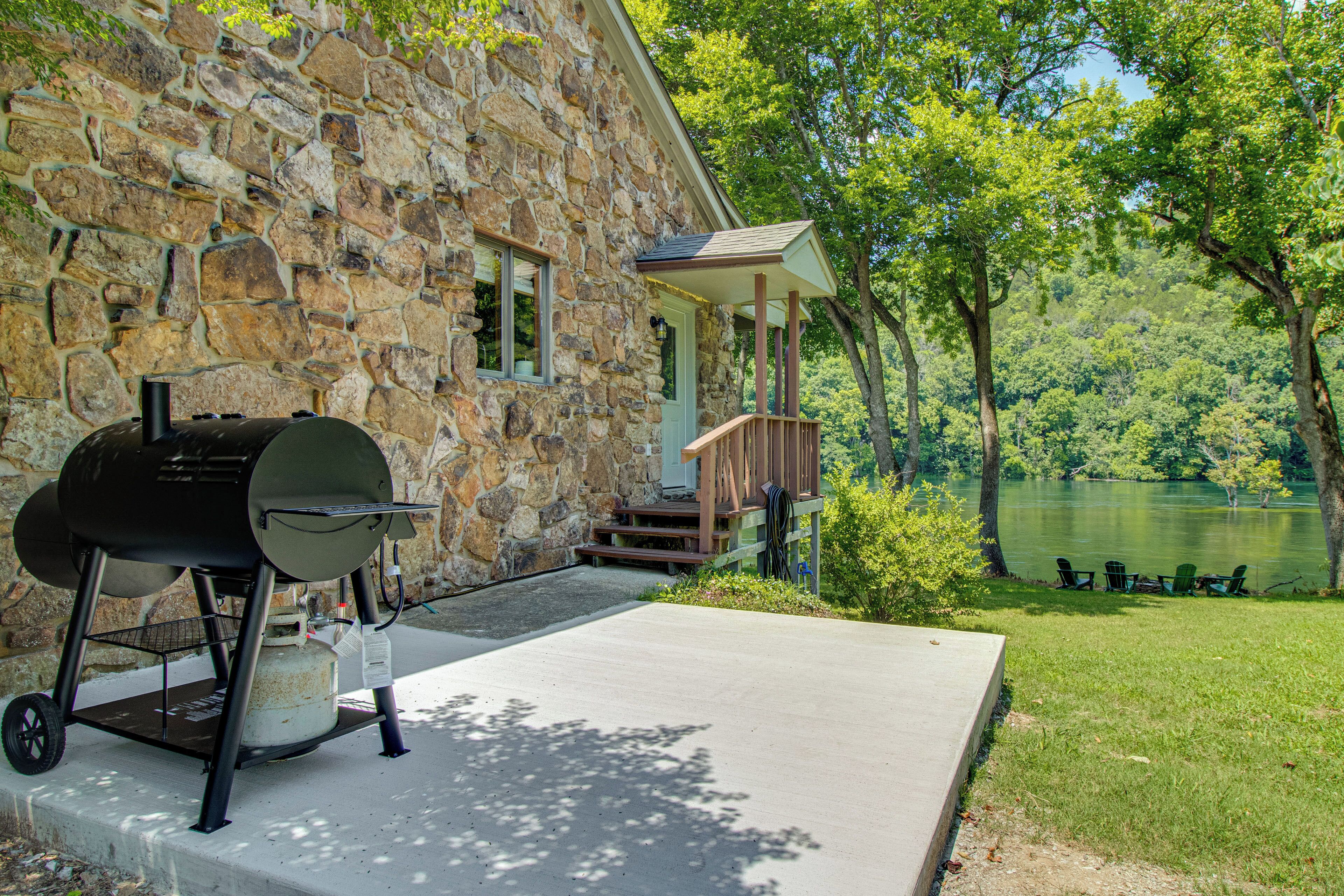 Une maison en pierre avec un barbecue, une véranda et une vue sur un lac.