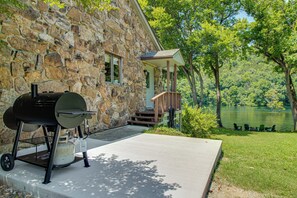 Una casa de piedra con una parrilla, un porche y vista al lago.
