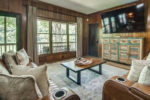 Ein Wohnzimmer mit großem Fenster, einem an der Wand befestigten Fernseher und einer Holzkommode mit Schubladen.