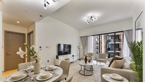 A modern living room with a dining area, a flat-screen TV, and a large window with a view of high-rise buildings. - Madely | Opulent Condo Act Two | Burj Khalifa (Dubai)