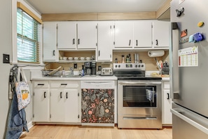 A compact kitchen with white cabinets, a dishwasher, a stove, and a refrigerator. - Walk to Village District! Charming Escape w/ Yard (Raleigh)