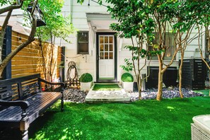 A bench, a door, a small garden with grass, and a tree. - Walk to Village District! Charming Escape w/ Yard (Raleigh)