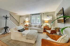 Ein modernes Wohnzimmer mit einer Couch, einem Couchtisch und einem braunen Ledersessel. Eine Treppe mit Garderobe und Pflanze ist ebenfalls zu sehen.
