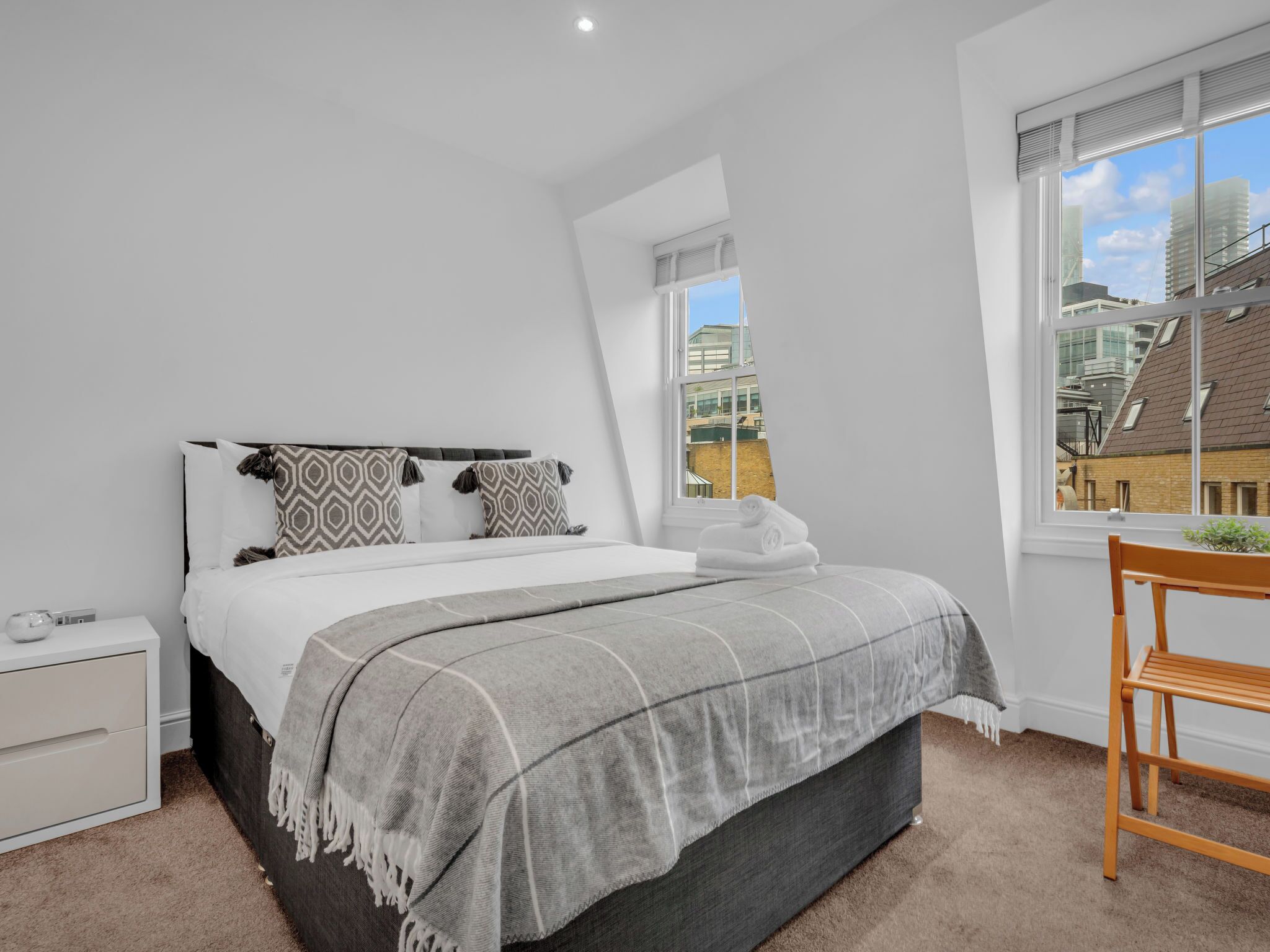 A bedroom with a bed, bedside table, and a window with a view of buildings.