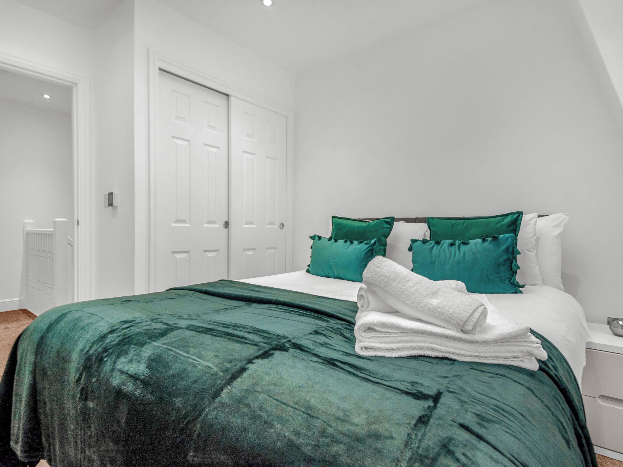 Un dormitorio con una cama, almohadas verdes, ropa de cama blanca y una puerta blanca.