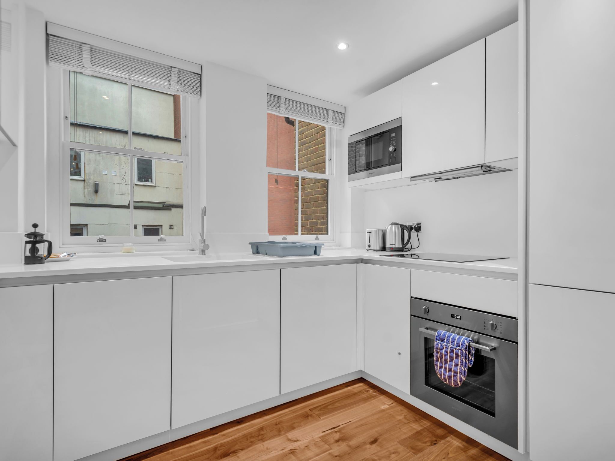 A modern kitchen with white cabinets, a built-in oven, a microwave, and a window with blinds.