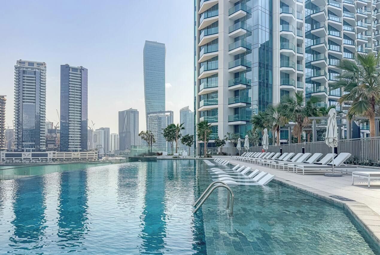 A swimming pool with lounge chairs and a city skyline in the background.