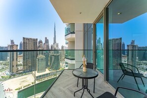 Ein Balkon mit Glasgeländer, einem Tisch mit Stühlen und Blick auf eine Stadtlandschaft mit einem hohen Gebäude.